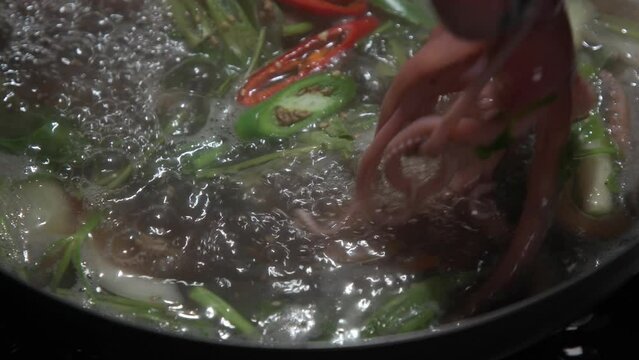 전골 냄비에 낚지와 야채가 담긴 끓고 있는 연포탕에서 집게로 낚지를 옮기는  