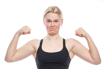 Teen girl funny shows her biceps. A cute blonde with freckles on her face in a sporty black top. Victory, activity and sport. White background. Close-up.