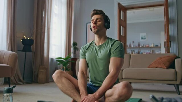 Peaceful athlete practicing meditation at home yoga mat in wireless headphones. 
