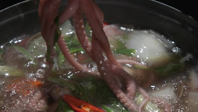 전골 냄비에 낚지와 야채가 담긴 끓고 있는 연포탕에서 집게와 가위로 낚지를 자르는 