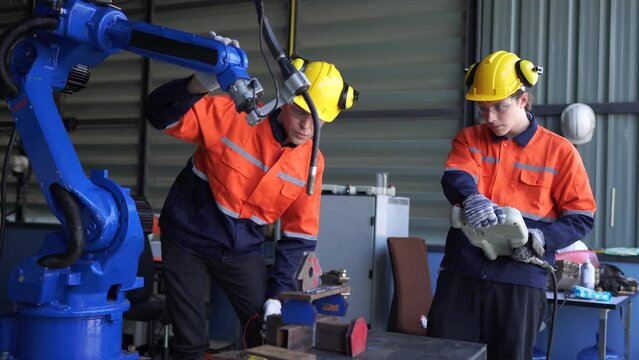 Factory engineers inspecting on machine with smart tablet. Worker works at heavy machine robot arm. The welding machine with a remote system in an industrial factory. Artificial intelligence concept.