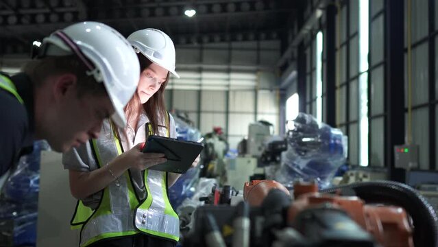 team engineers inspecting on machine with smart tablet. Worker works at heavy machine robot arm. The welding machine with a remote system in an industrial factory. Artificial intelligence concept.