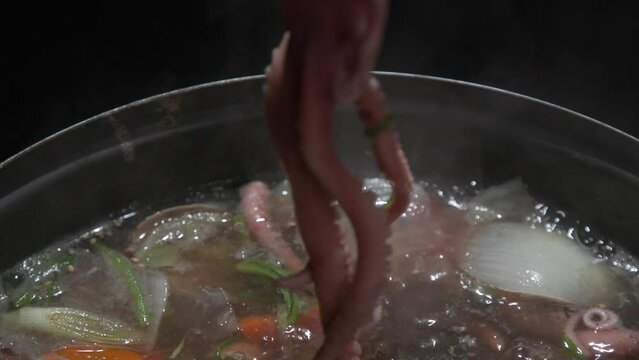 전골 냄비에 낚지와 야채가 담긴 끓고 있는 연포탕에서 집게와 가위로 낚지를 자르는 