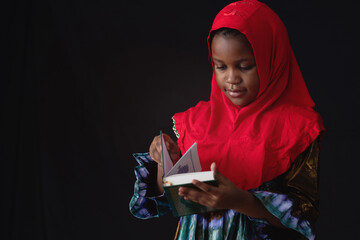 African Muslim little girl in traditional costume interested and reads the Quran, black background