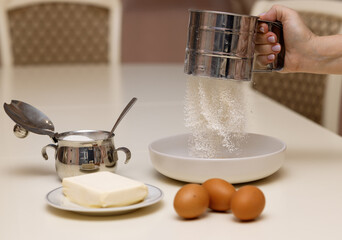 Sifting flour before kneading cookie dough. The ingredients for the dough are on the table