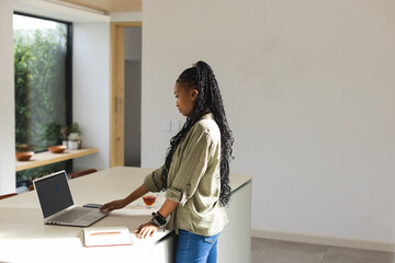 A young African American woman stands at a white table with a laptop, with copy space