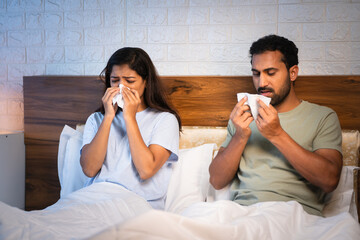 Sick Indian couples sneezing at night while sleeping at night due to cold or cough on bedroom -...