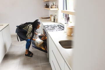 A young African American woman checks on food in an oven with copy space