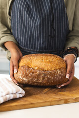 A young African American woman holds a freshly baked loaf of bread with copy space