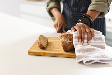 A person slices bread on a wooden cutting board, with a towel nearby, with copy space
