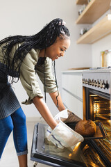 A young African American woman takes a loaf of bread out of an oven