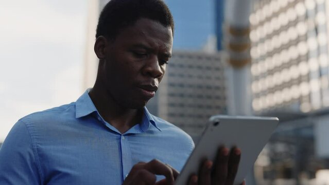 African American Handsome Thoughtful Entrepreneur Distance Working Using Digital Tablet. Serious Boss Chatting with Coworkers while Standing Outside in Business District. People and Technology Concept