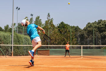 Boy playing tennis with his coach on a dirt court