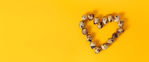 Symbol of love. Heart shape made of marble quail eggs on yellow background. Easter holiday....