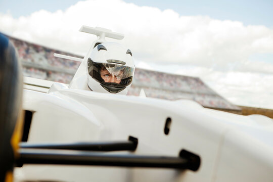 Focused racing driver in helmet sitting in a white racecar at the track. 