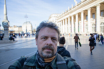 man in city center taking phone selfie photo in bordeaux town front theater opera