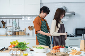 portrait of loving young loving couple asian of wife tie up apron standing a cheerful preparing food and enjoy cook cooking with vegetables, meat, bread while standing on a kitchen Condo life or home
