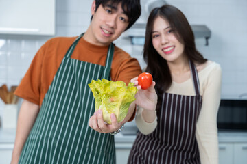 Happy portrait of loving young loving couple asian of having fun standing a cheerful preparing food and enjoy cook cooking with vegetables, meat, bread while standing on a kitchen Condo life or home