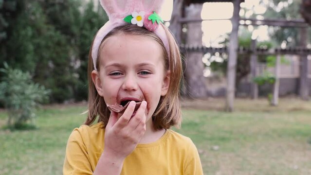 Easter egg hunt. Excited emotion surprise adorable child girl with dirty mustache mouth in bunny ears rabbit costume hold and eat Easter chocolate egg. Children positive emotions. Kid happy Easter