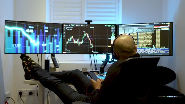 A man sits comfortably in front of three interconnected computer screens, representing the idea of engaging in home-based or day-trading activities.