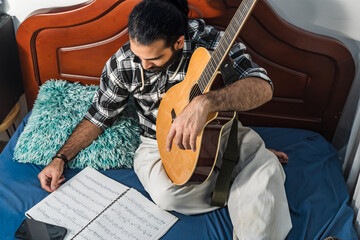 Colombian man reading sheet music and studying guitar. Acoustic and harmonic instrument