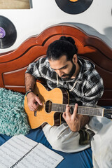 Colombian man playing and studying guitar in his room. Acoustic and harmonic instrument.