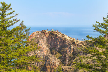 Baikal Lake on sunny summer day. Tourists climb to rocky Cape Shunte Left or as it is also called, Cape of Love on Olkhon Island and take pictures of beautiful landscape. Travel and outdoor activities