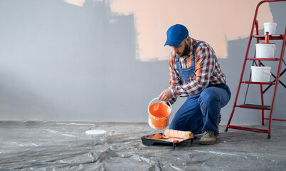 Male decorator pouring orange paint into tray indoors, close-up. Home renovation concept.