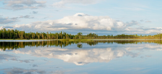 Calm evening by a small lake with reflections on the water surface and beautiful clouds in the sky, Northern Finland