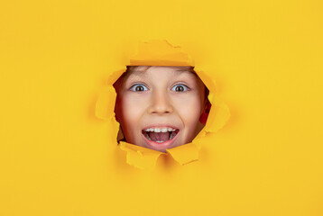 Kid with toothy smile shows face in paper hole. Portrait of beautiful happy smiling little boy...