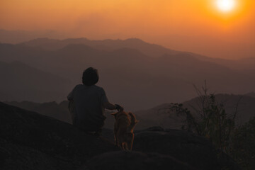 Obraz premium landscape and travel concept with solo freelancer man relax and play with dog at top of mountain and sunset with layer of mountain