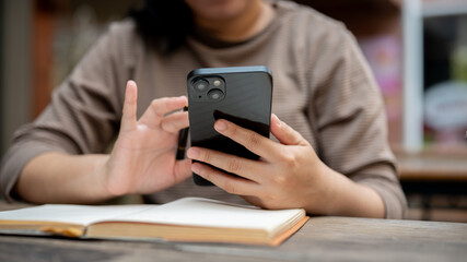 A cropped shot of an Asian woman using her smartphone while reading a book or doing some work.