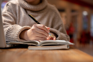 A woman in a comfy sweater is working remotely at a cafe, making list in her notebook.