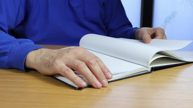 Hand turns blank pages of diary four times, front view of senior man in blue t-shirt, copy space.