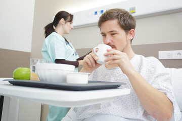 male patient in hospital bed eating meal from tray