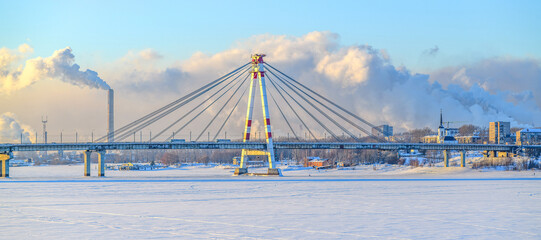 Obraz premium Panoramic view of the silhouette first cable-stayed bridge in Russia across the Sheksna River in Cherepovets in selective focus against the backdrop of thick toxic smoke from a metallurgical plant.