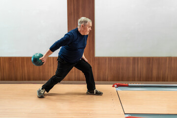Elderly man poised to roll bowling ball in leisurely game, active senior lifestyle.