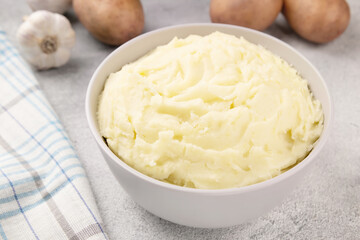 Bowl of tasty mashed potato, parsley,  and pepper on grey marble table