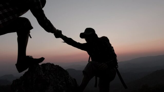 silhouette of Hikers climbing on rock, mountain at sunset, one of them giving hand and helping to climb. support, help and success concept,  Leadership Concept, teamwork.