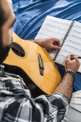 Colombian man playing guitar and studying sheet music in his room. Acoustic and harmonic instrument