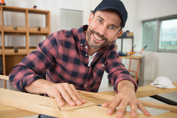 happy male carpenter sanding wood in his workshop