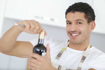 man in apron opening bottle of wine