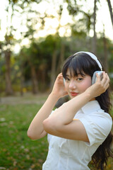 Portrait of attractive young Asian woman listening music with headphones in city park