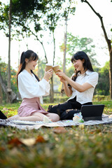 Two happy young women sitting on a picnic blanket and drinking coffee