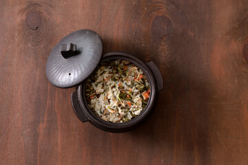 Rice with vegetables in a pot on a wooden background. Top view