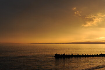 Sunset over the sea or ocean with a breakwater and clouds