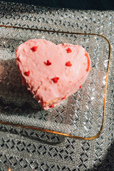 small pink heart shaped cake with red heart sprinkles on glass tray with sparkly silver background