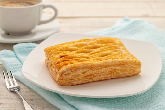 A baked pineapple pie in small size served on a square white serving plate together with a cup of coffee for a coffee break.