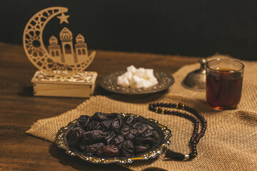 Glass of tea with sugar and dried dates on a wooden background with burlap. Ramadan Kareem holiday background. Halal meal set for fasting is obligatory for Muslim on wooden.  Soft focus. Shallow DOF.