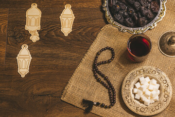 Glass of tea with sugar and dried dates on a wooden background with burlap. Ramadan Kareem holiday background. Halal meal set for fasting is obligatory for Muslim on wooden.  Soft focus. Shallow DOF.